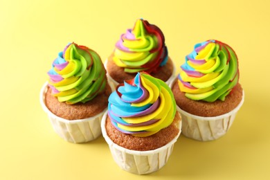 Photo of Tasty cupcakes with colorful cream on yellow background, closeup