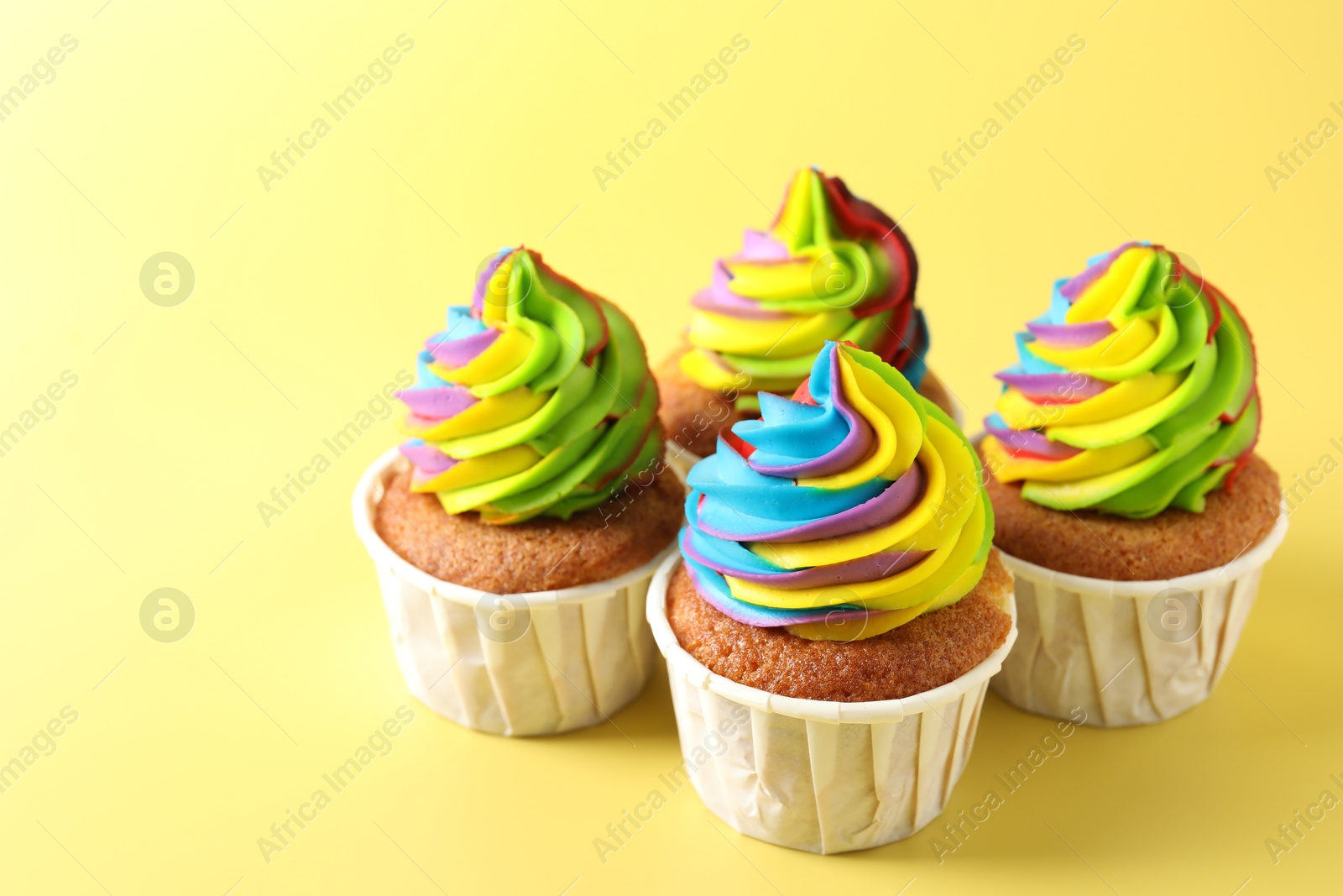 Photo of Tasty cupcakes with colorful cream on yellow background, closeup