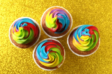 Photo of Tasty cupcakes with colorful cream on shiny golden background, flat lay