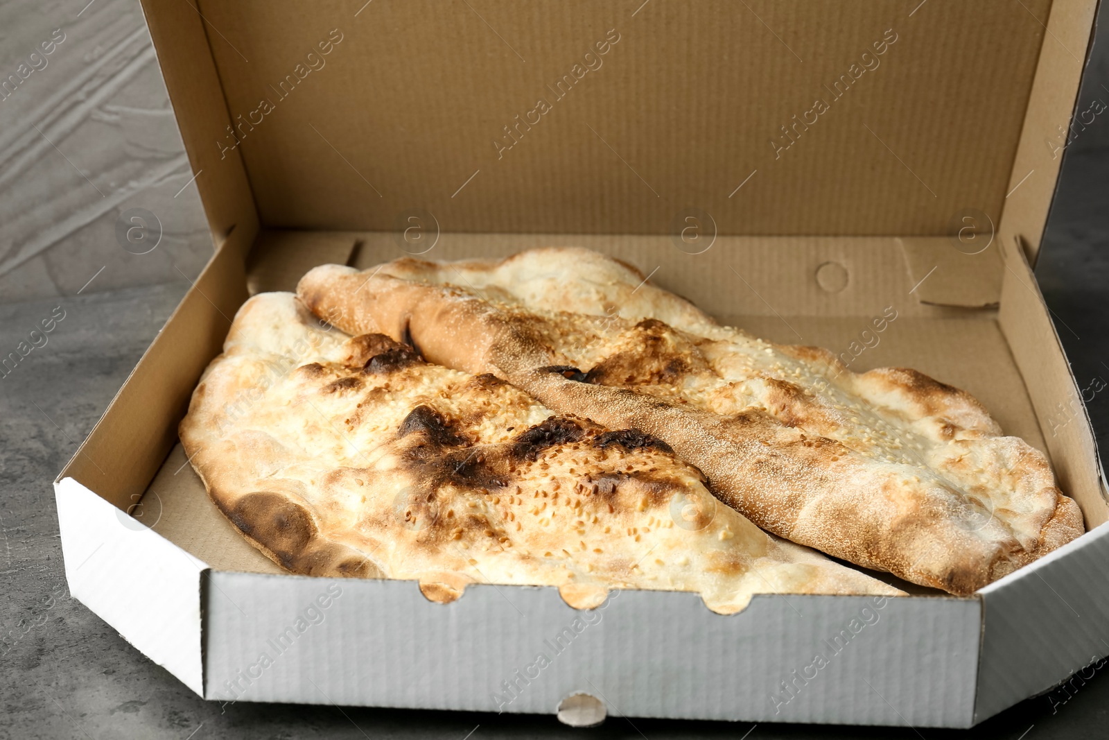 Photo of Delicious calzones in cardboard box on grey textured table, closeup