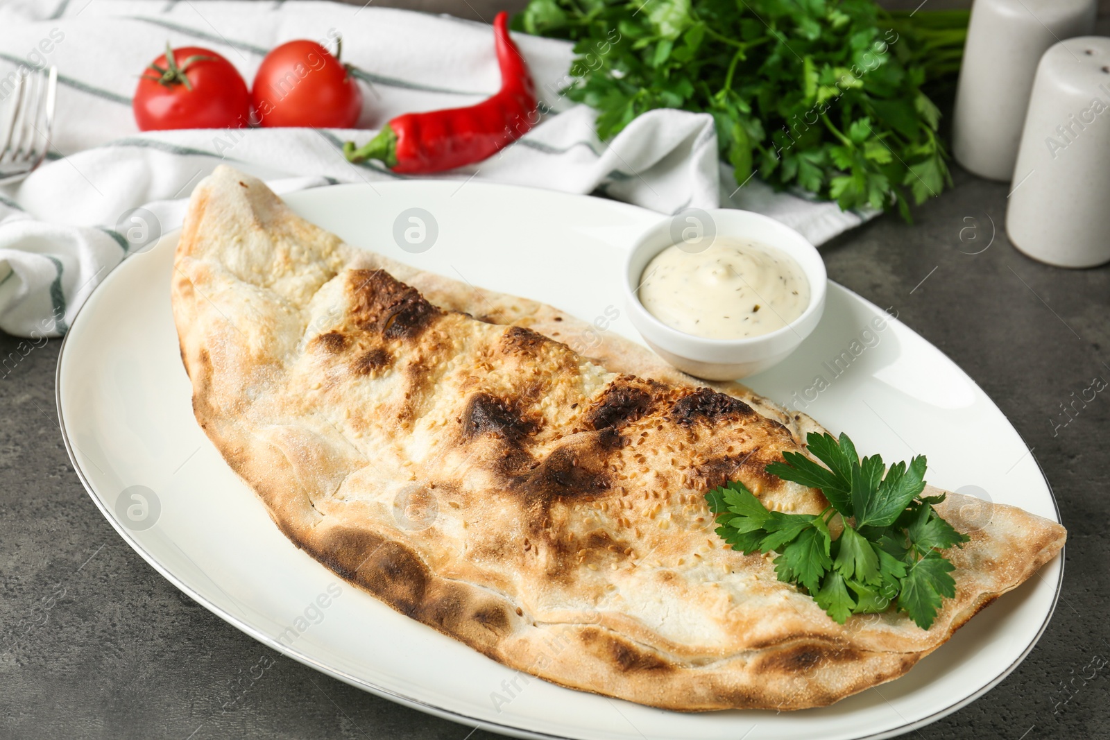 Photo of Delicious calzone served with sauce on grey table, closeup