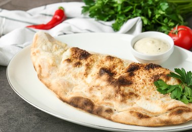 Photo of Delicious calzone served with sauce on grey table, closeup