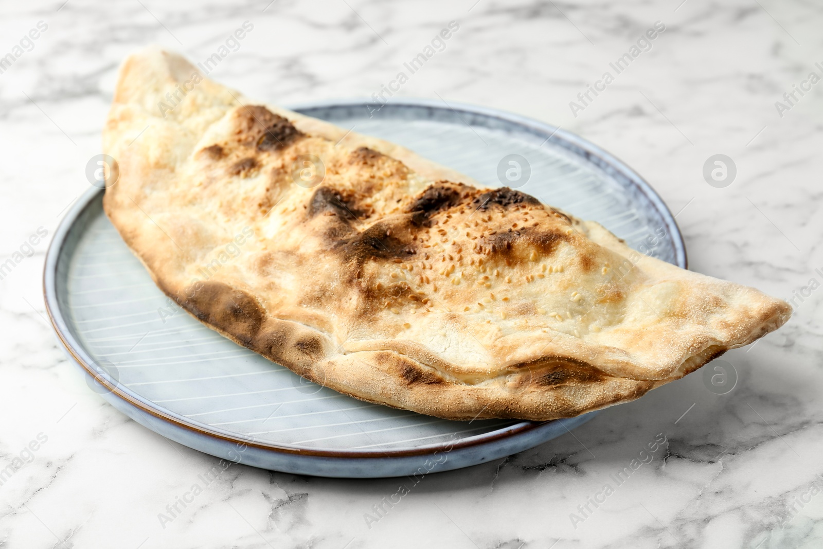 Photo of Delicious calzone on white marble table, closeup