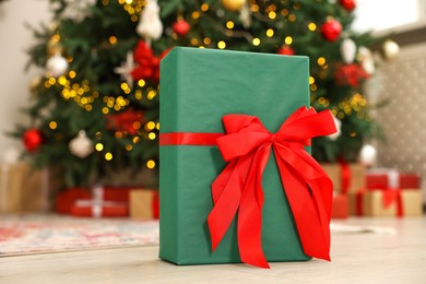 Photo of Gift box with bow near Christmas tree in room, selective focus