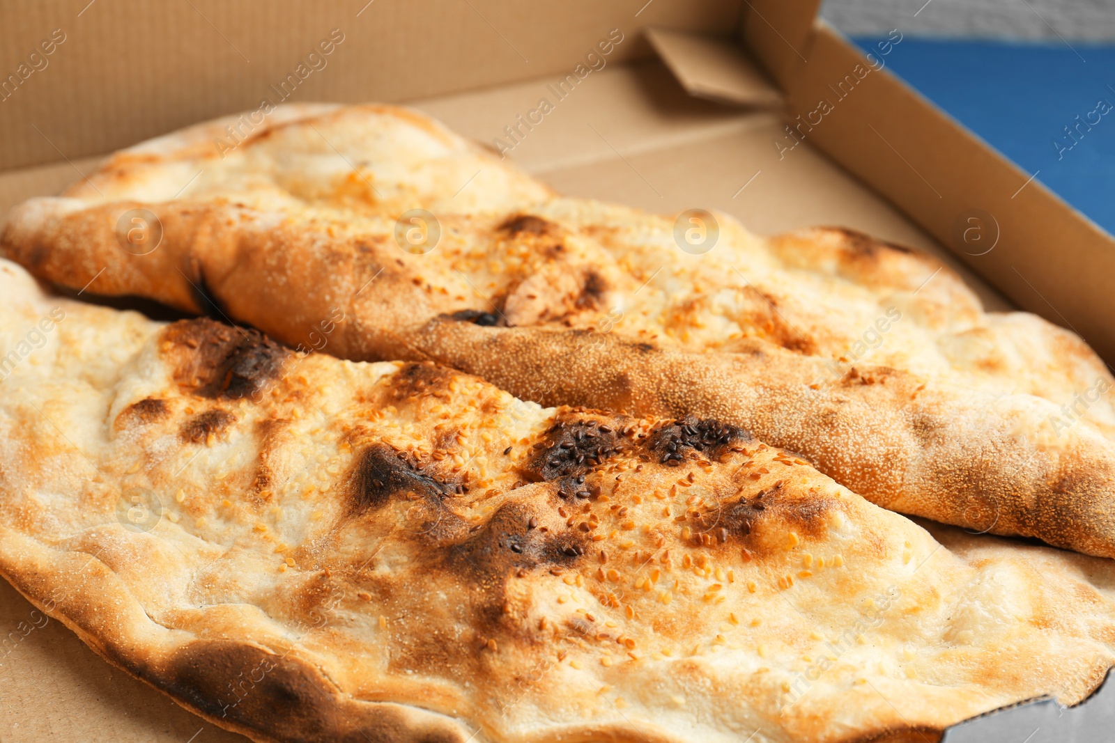 Photo of Tasty calzones in cardboard box on blue table, closeup