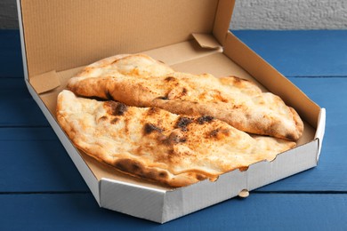 Photo of Tasty calzones in cardboard box on blue wooden table, closeup