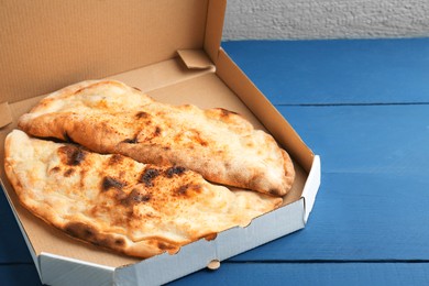 Photo of Tasty calzones in cardboard box on blue wooden table, closeup