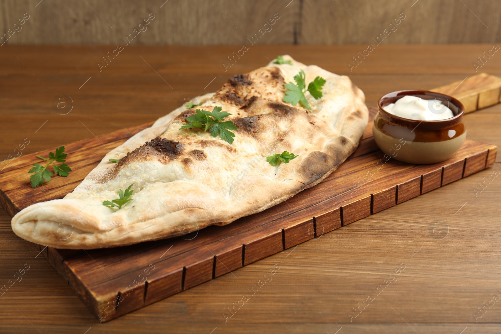 Photo of Board with tasty calzone, parsley and sauce on wooden table, closeup