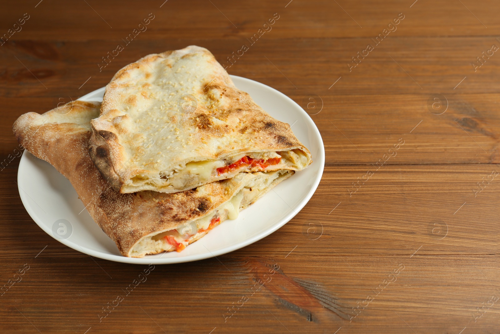 Photo of Halves of tasty calzone with meat, cheese and tomato on wooden table, closeup. Space for text