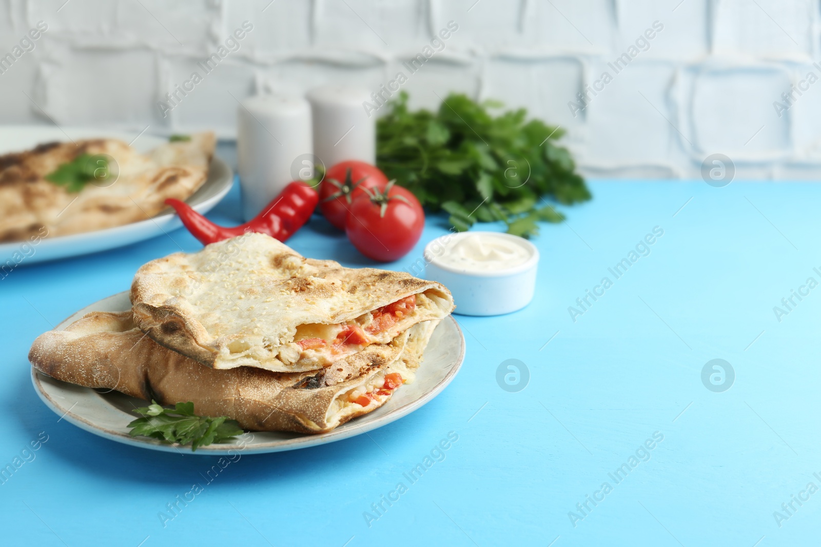 Photo of Halves of tasty calzone with meat, cheese, tomato and sauce on light blue table. Space for text