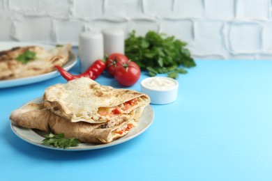 Photo of Halves of tasty calzone with meat, cheese, tomato and sauce on light blue table. Space for text