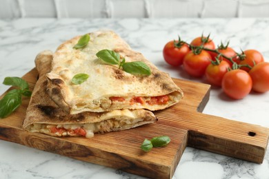 Photo of Halves of tasty calzone with meat, cheese, basil and tomato on white marble table, closeup