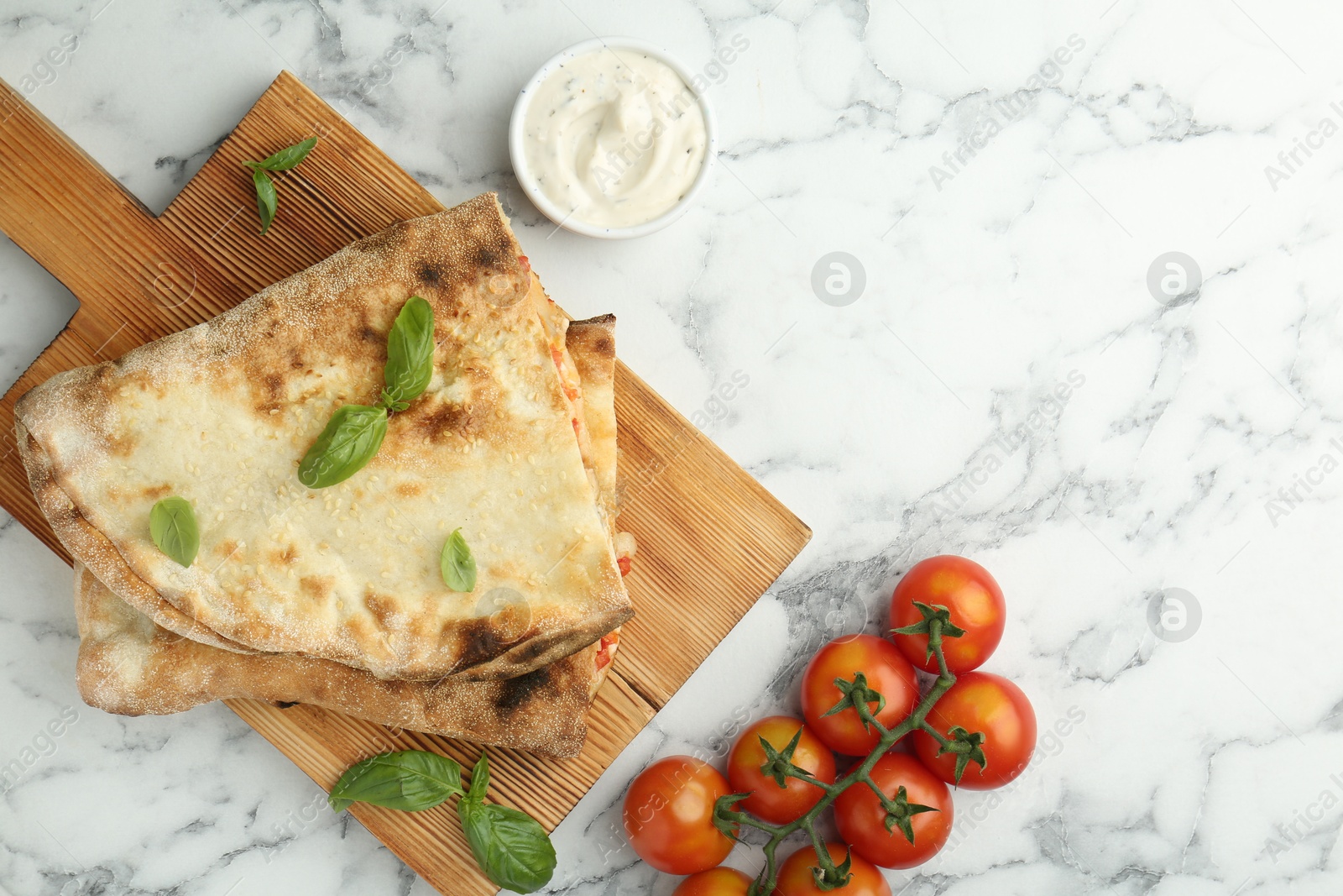 Photo of Halves of tasty calzone, basil, sauce and tomato on white marble table, flat lay. Space for text