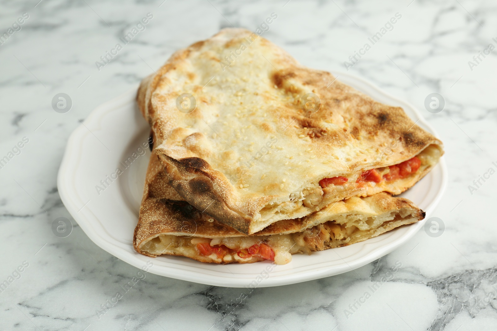 Photo of Halves of tasty calzone with meat, cheese and tomato on white marble table, closeup