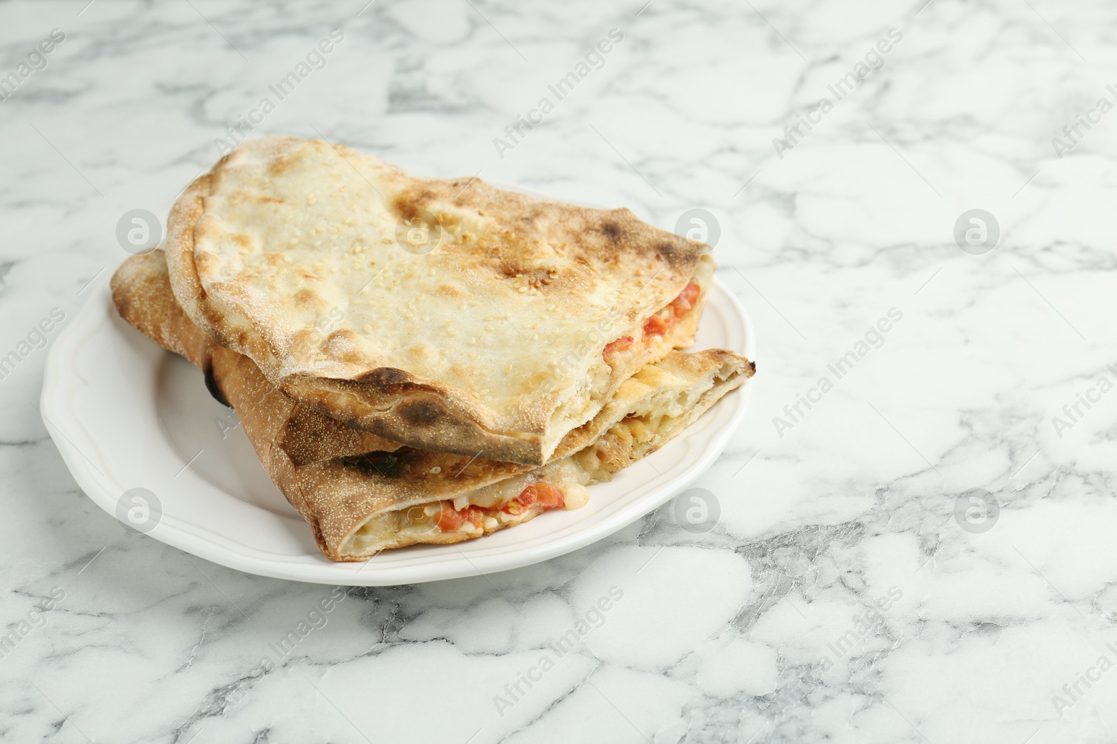 Photo of Halves of tasty calzone with meat, cheese and tomato on white marble table, closeup. Space for text