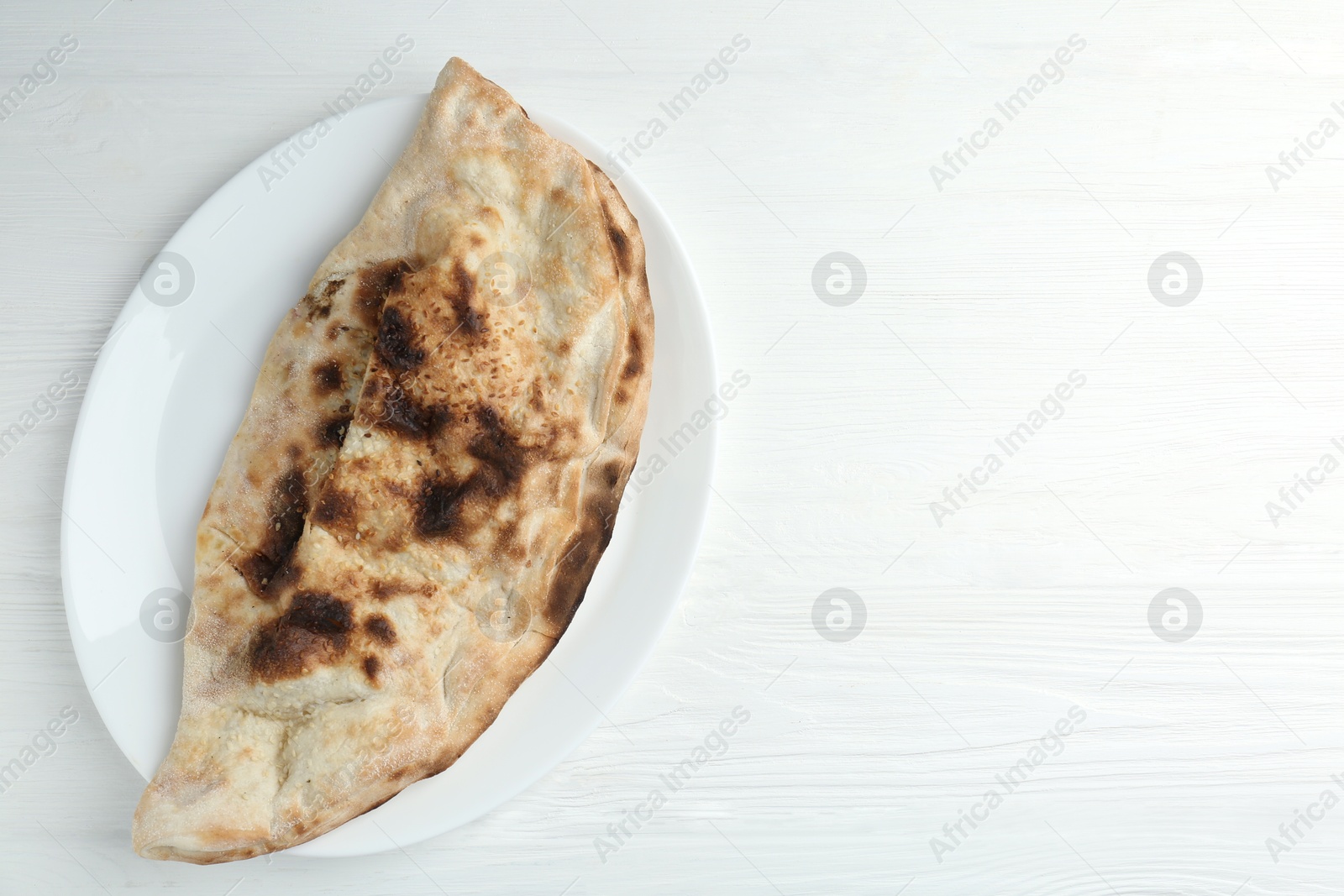 Photo of Plate with tasty calzone on white wooden table, top view. Space for text