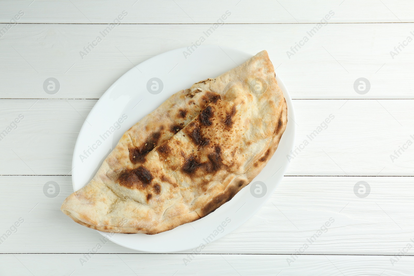 Photo of Plate with tasty calzone on white wooden table, top view