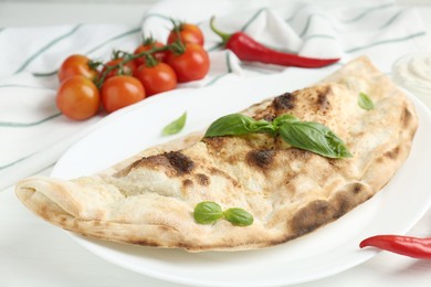 Photo of Tasty calzone, basil, chili pepper and tomatoes on white wooden table, closeup