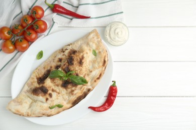 Photo of Tasty calzone, basil, chili pepper, sauce and tomatoes on white wooden table, flat lay. Space for text