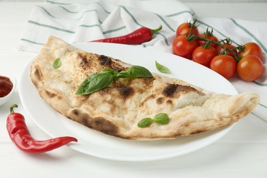 Photo of Tasty calzone, basil, chili pepper, sauce and tomatoes on white wooden table, closeup