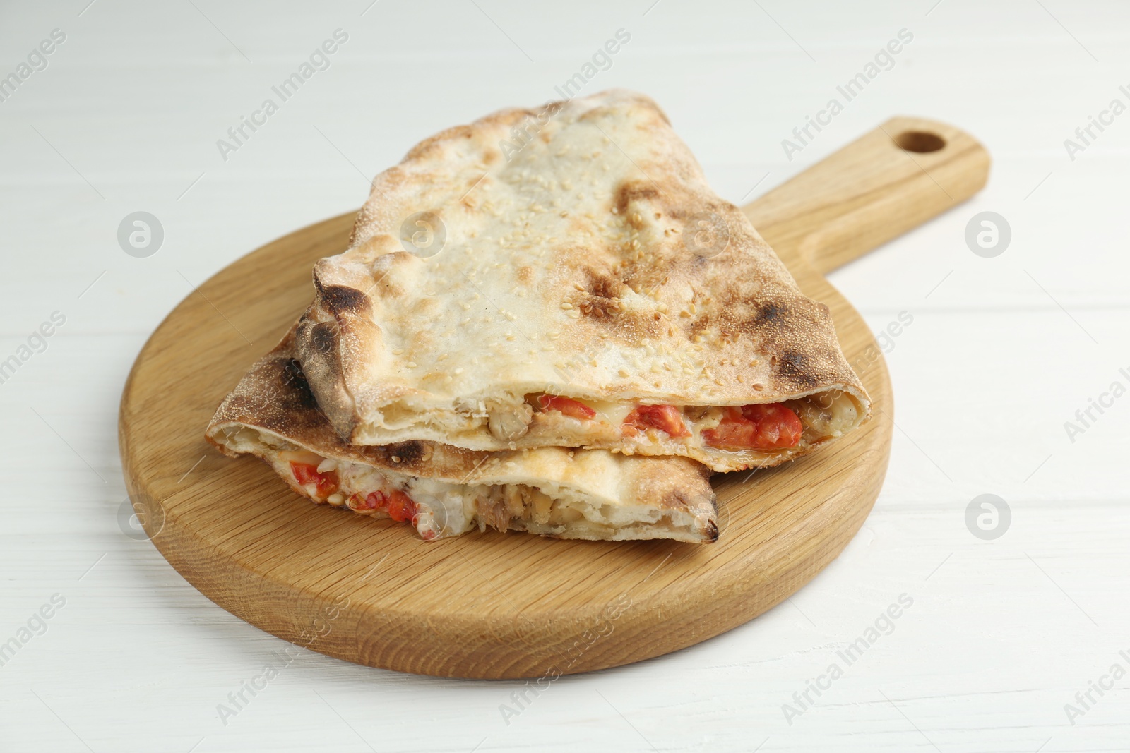 Photo of Halves of tasty calzone with meat, cheese and tomato on white wooden table, closeup