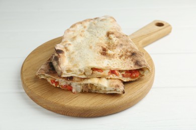 Photo of Halves of tasty calzone with meat, cheese and tomato on white wooden table, closeup