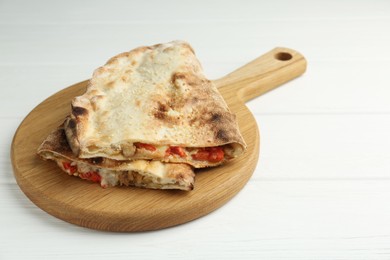 Photo of Halves of tasty calzone with meat, cheese and tomato on white wooden table, closeup