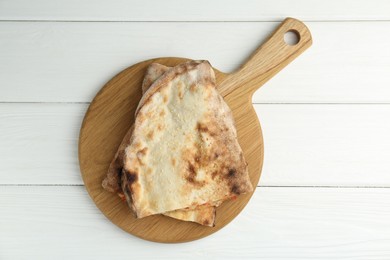 Photo of Board with halves of tasty calzone on white wooden table, top view