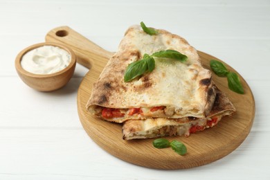 Photo of Halves of tasty calzone with meat, cheese, tomato, basil and sauce on white wooden table, closeup