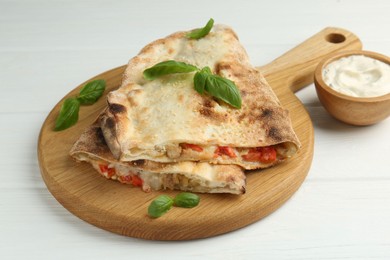 Photo of Halves of tasty calzone with meat, cheese, tomato, basil and sauce on white wooden table, closeup