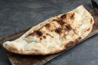 Photo of Board with tasty calzone on grey textured table, closeup