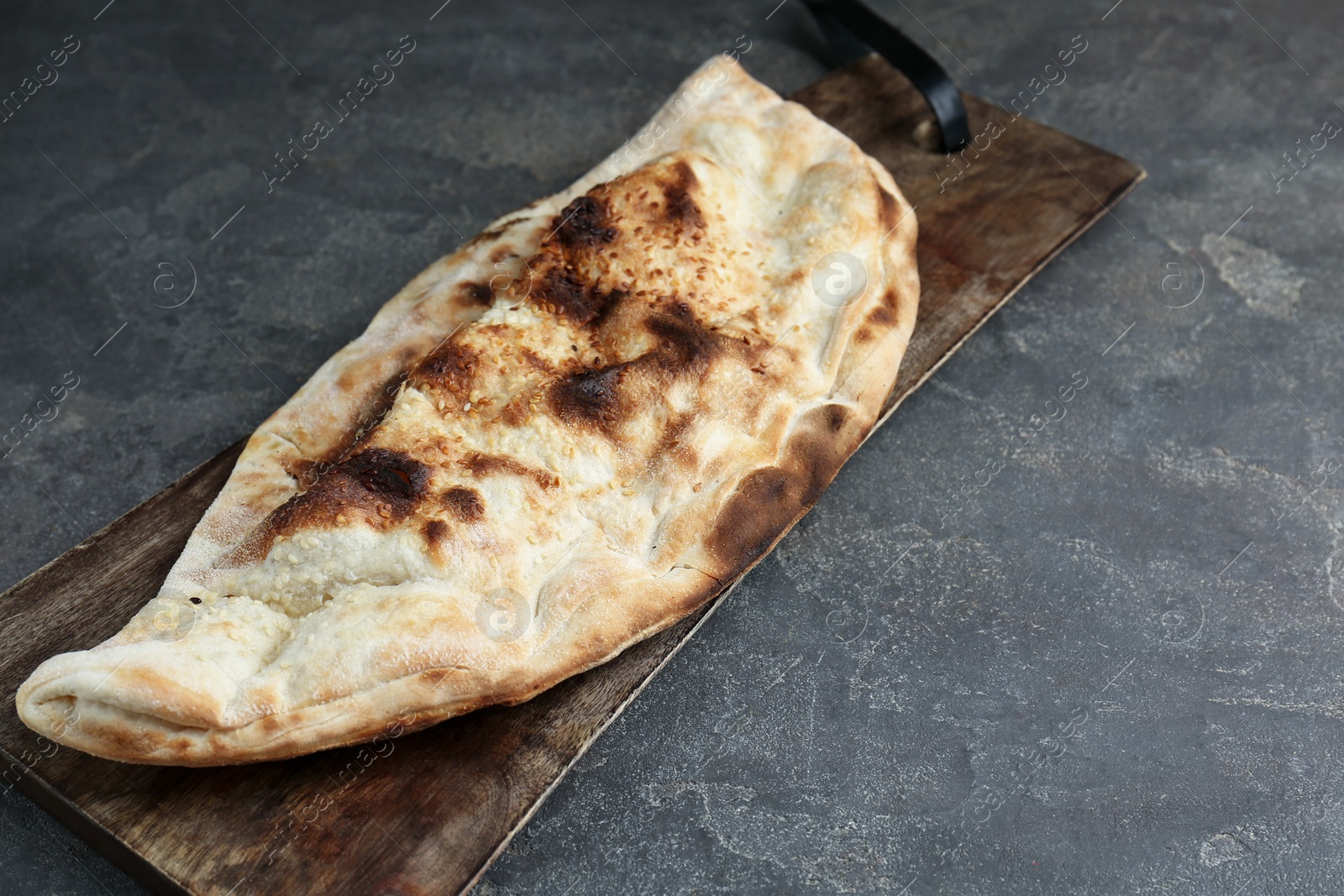 Photo of Board with tasty calzone on grey textured table, closeup