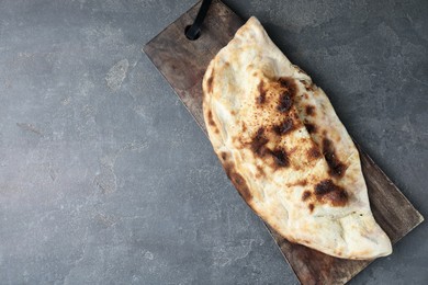 Photo of Board with tasty calzone on grey textured table, top view. Space for text