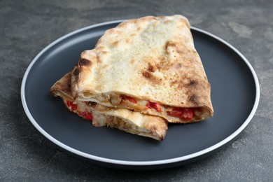 Photo of Halves of tasty calzone with meat, cheese and tomato on grey textured table, closeup