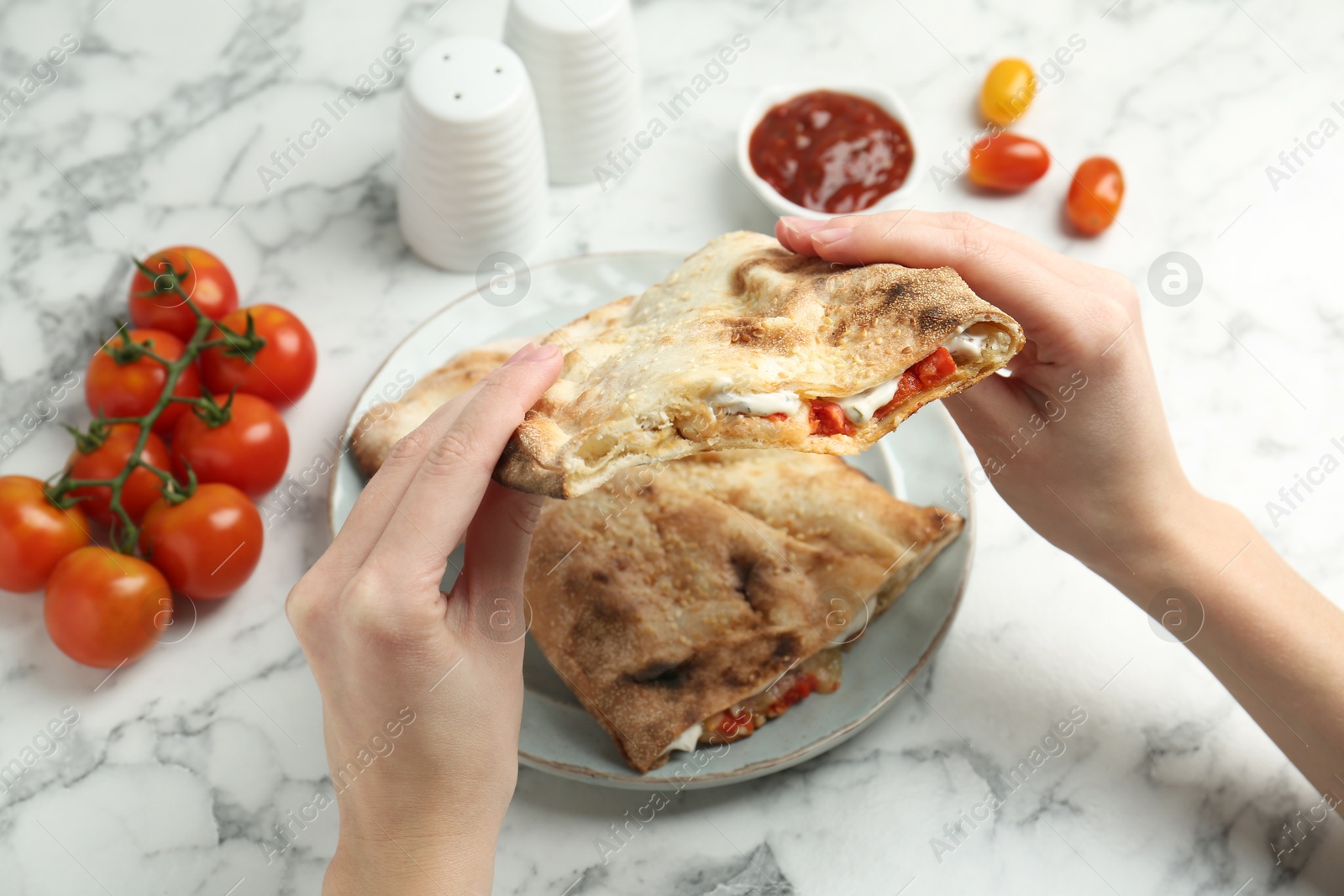 Photo of Woman eating tasty calzone with meat, cheese and tomato at white marble table, closeup