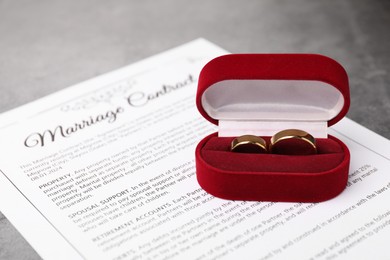 Photo of Marriage contract and golden rings on grey table, closeup