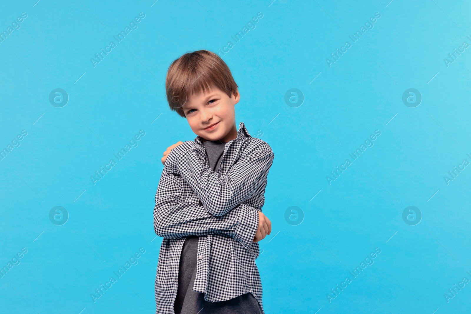 Photo of Cute little boy hugging himself on light blue background