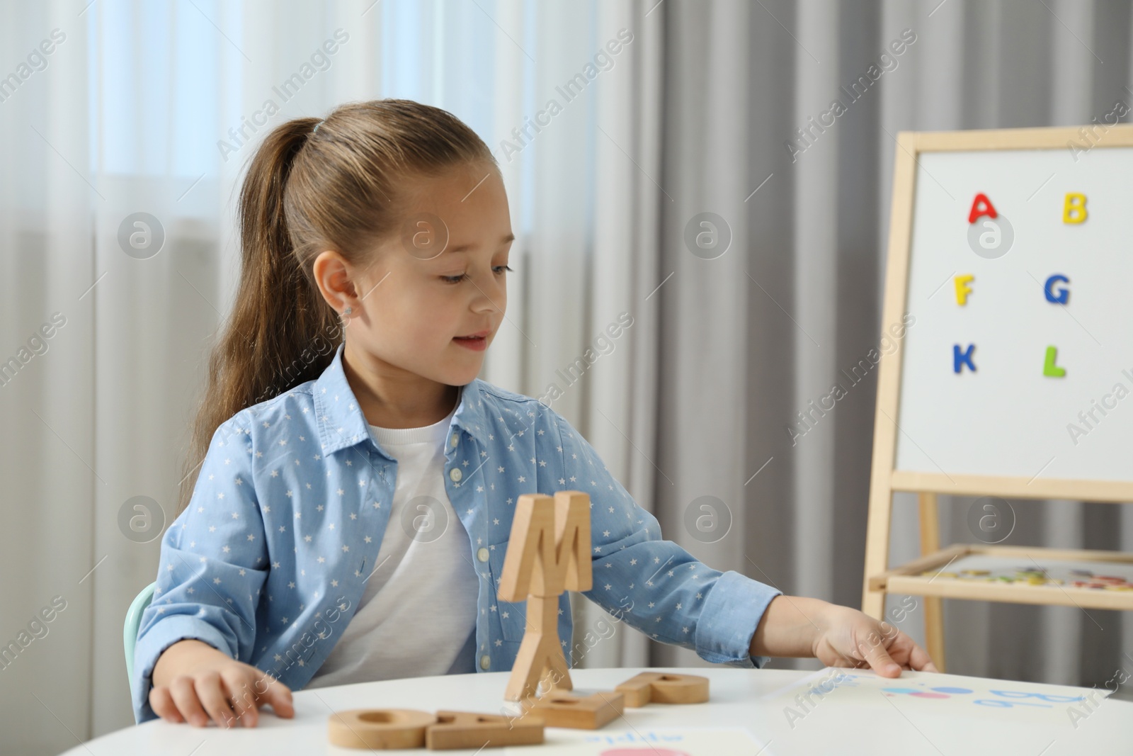 Photo of Little girl learning alphabet with wooden letters at white table indoors