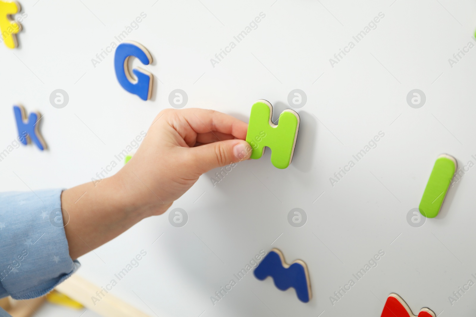 Photo of Little girl learning alphabet with magnetic letters on board, closeup