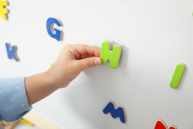 Photo of Little girl learning alphabet with magnetic letters on board, closeup