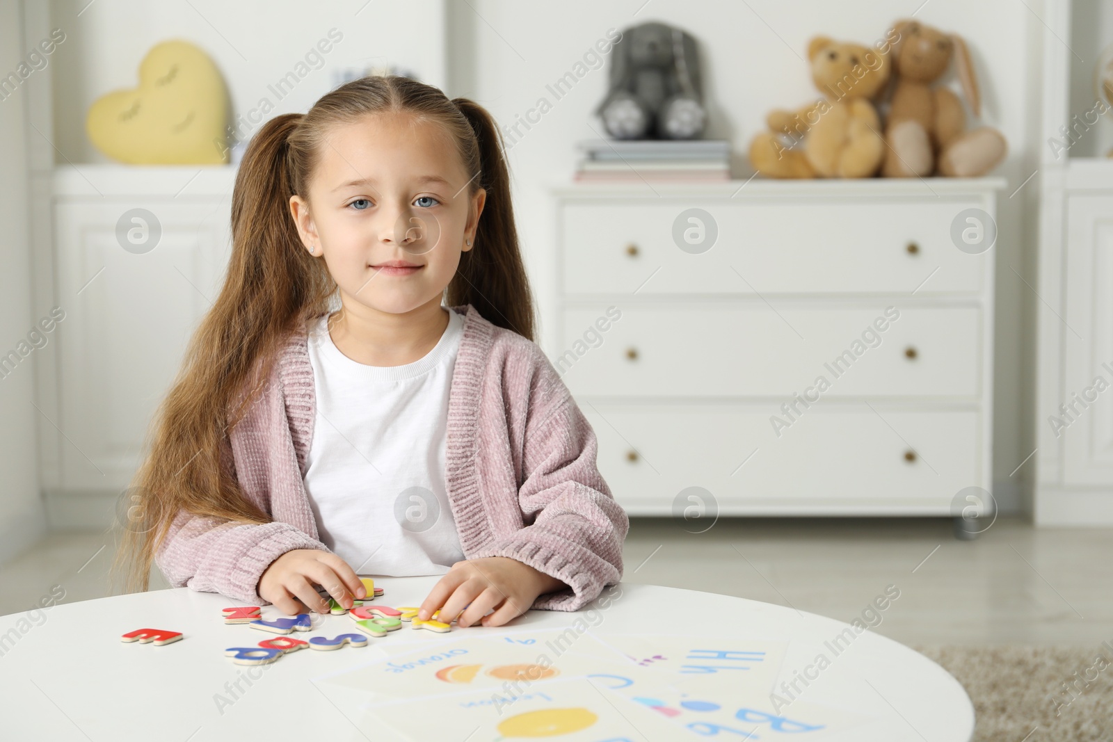 Photo of Little girl learning alphabet with magnetic letters at white table indoors, space for text