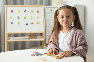 Photo of Little girl learning alphabet with different letters at white table indoors