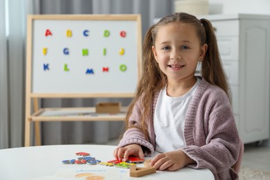 Photo of Little girl learning alphabet with different letters at white table indoors