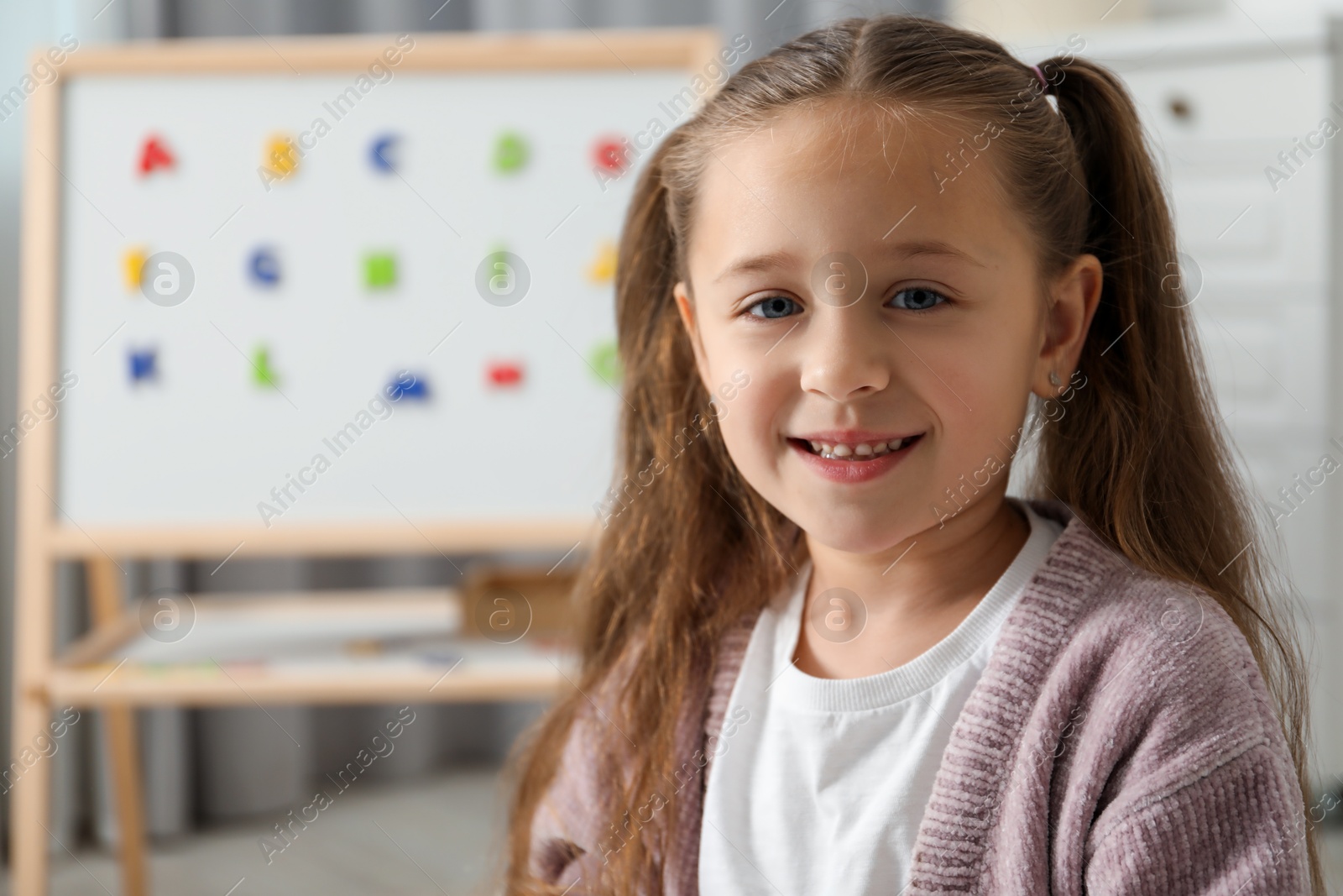 Photo of Little girl near board with magnetic letters indoors. Learning alphabet