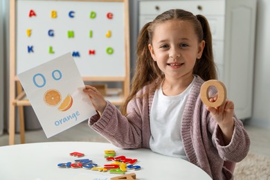 Photo of Little girl learning alphabet with different letters and picture at white table indoors