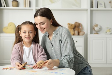 Photo of Speech therapist teaching little girl alphabet with different letters at white table indoors