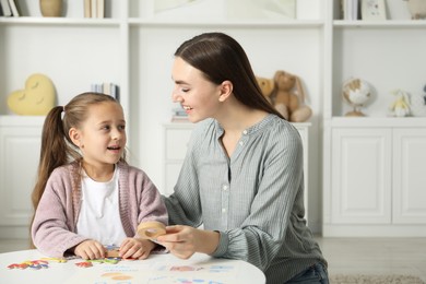 Photo of Speech therapist teaching little girl alphabet with different letters at white table indoors