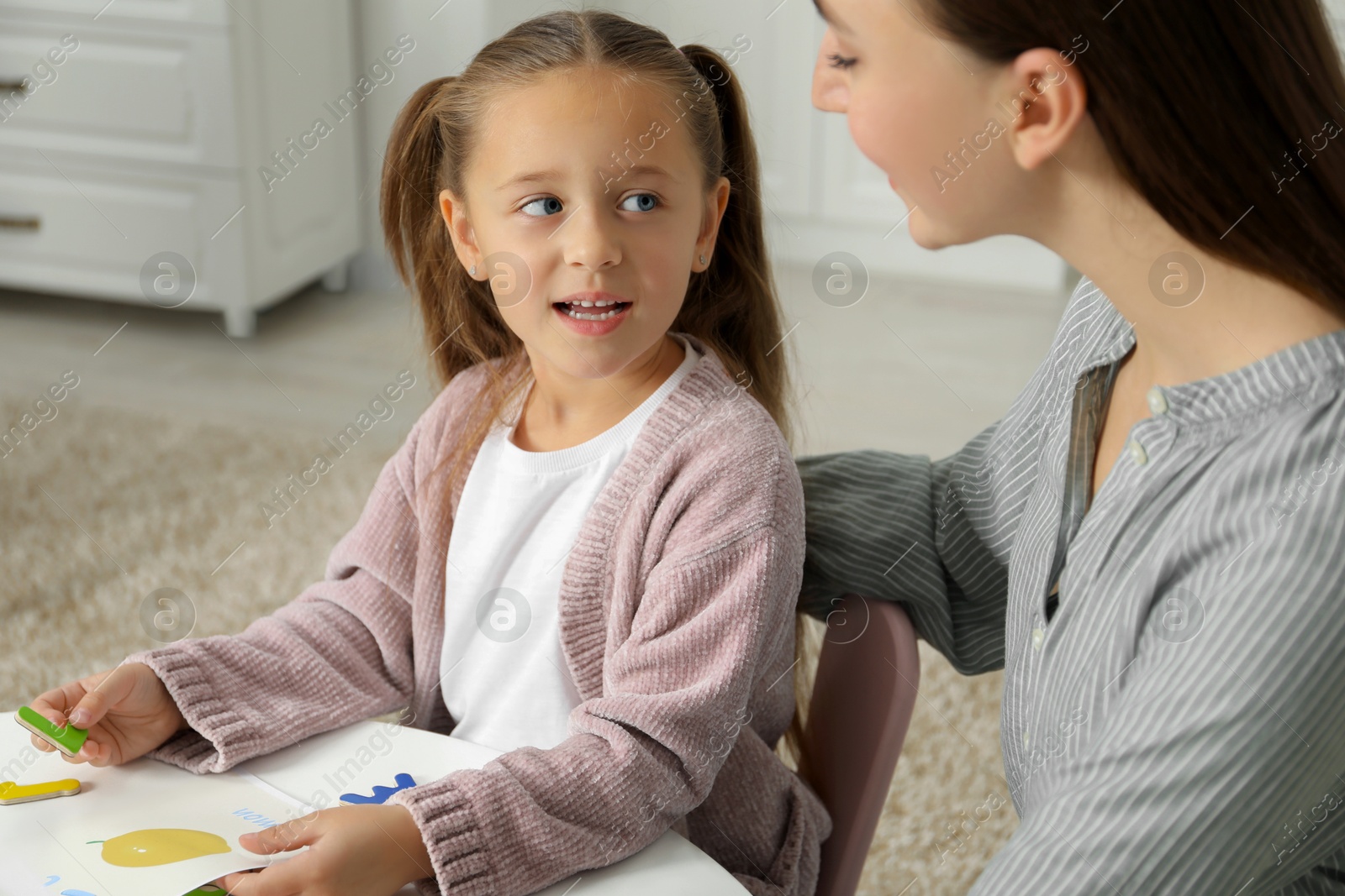 Photo of Speech therapist teaching little girl alphabet at table indoors