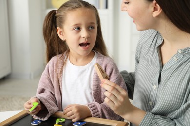 Photo of Speech therapist teaching little girl alphabet with different letters indoors, closeup