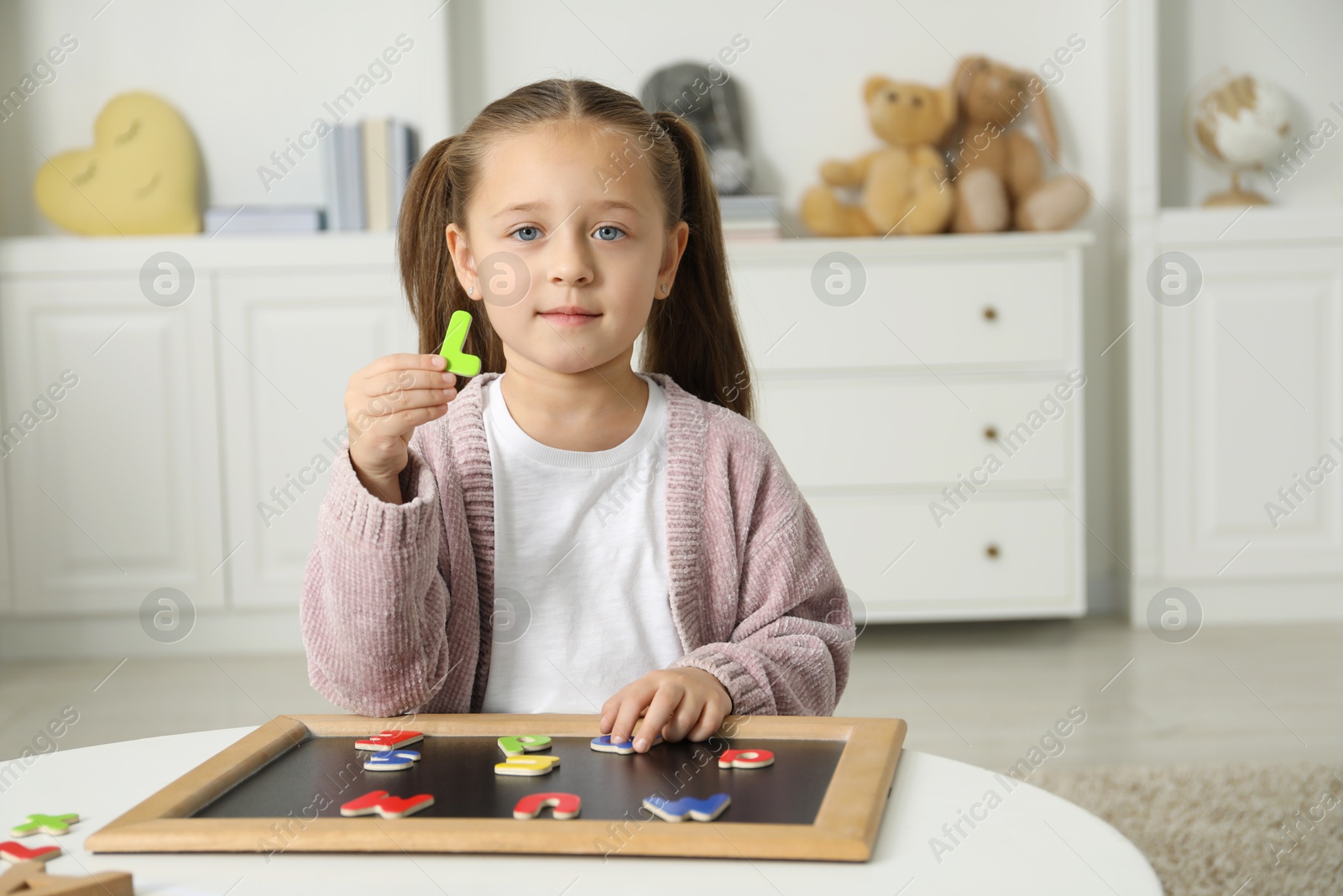 Photo of Little girl learning alphabet with magnetic letters at white table indoors